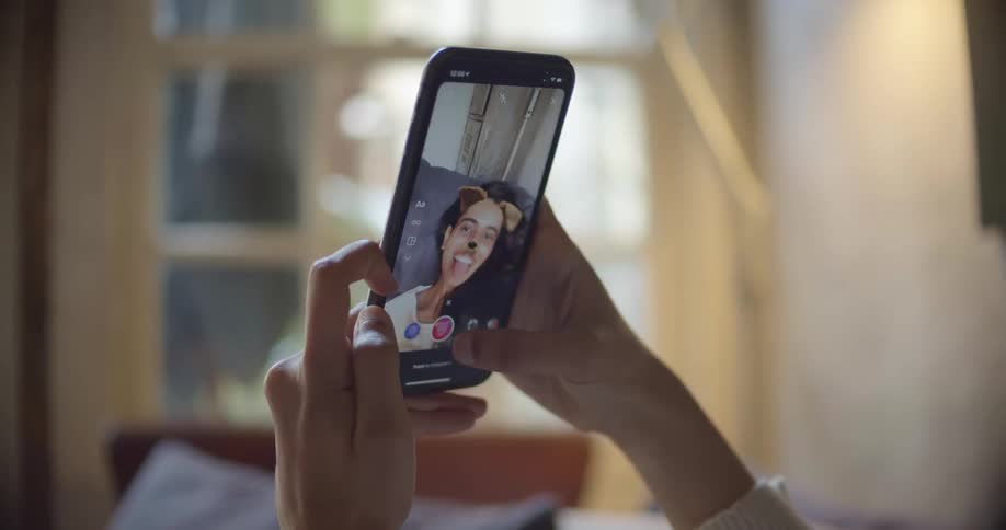 A woman holding a smartphone saves a photo of herself with filters added