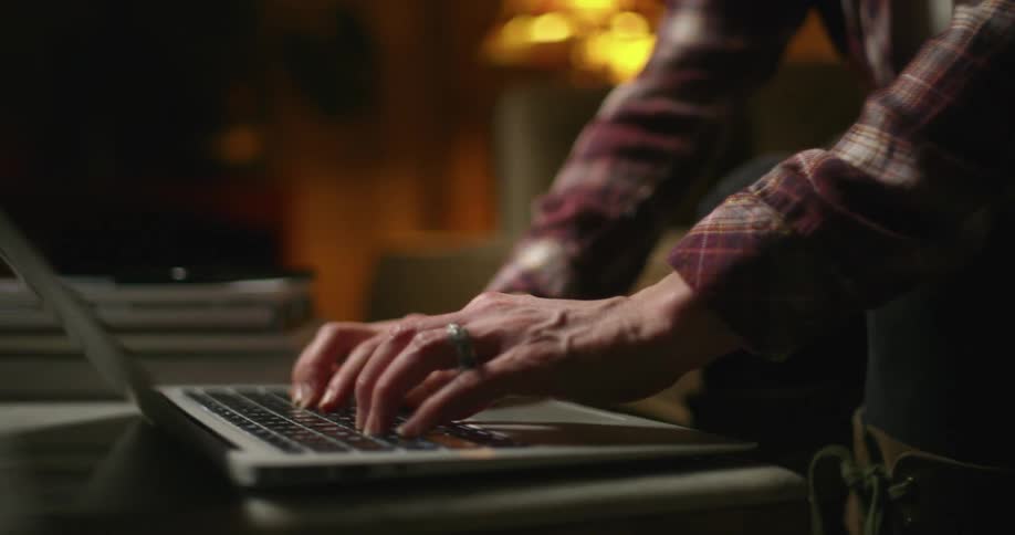 A woman sitting on a couch at home at night typing on a laptop computer on a coffee table