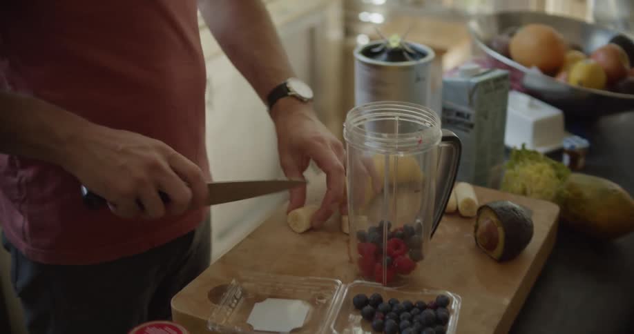Slicing banana and adding blueberries to a nutri bullet while preparing a smoothie