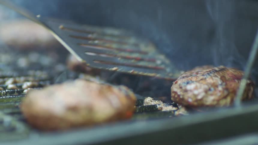 A spatula moving hamburgers on a grill with fire and smoke