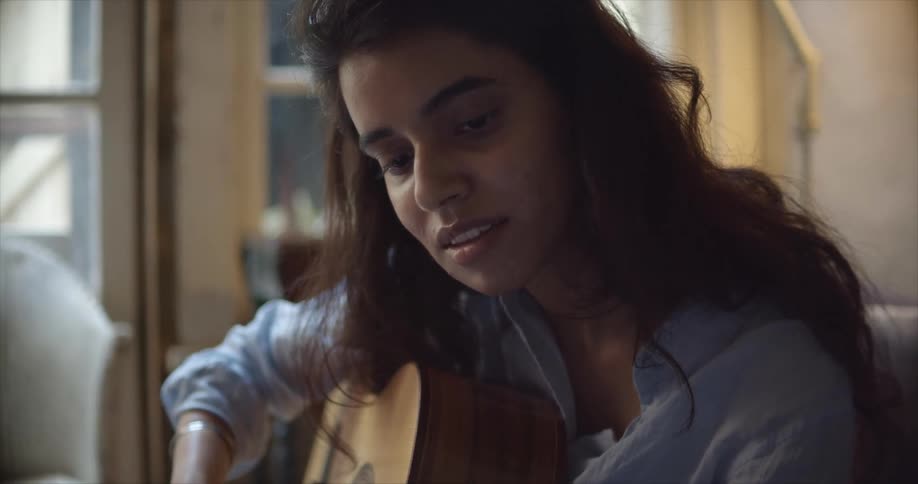 A woman is playing the guitar and sitting indoors