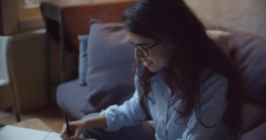 A woman is sitting on a couch and writing in a notebook