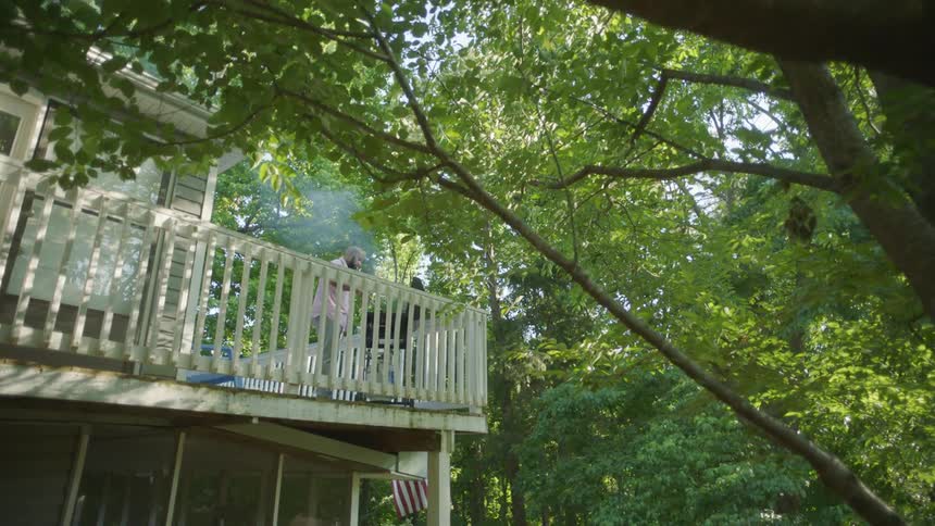 Man grilling a barbecue outdoors on the second floor deck of a house at daytime
