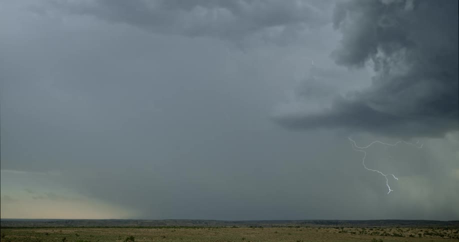 Lightning streaking arcs flashing across storm clouds hitting the ground over a field