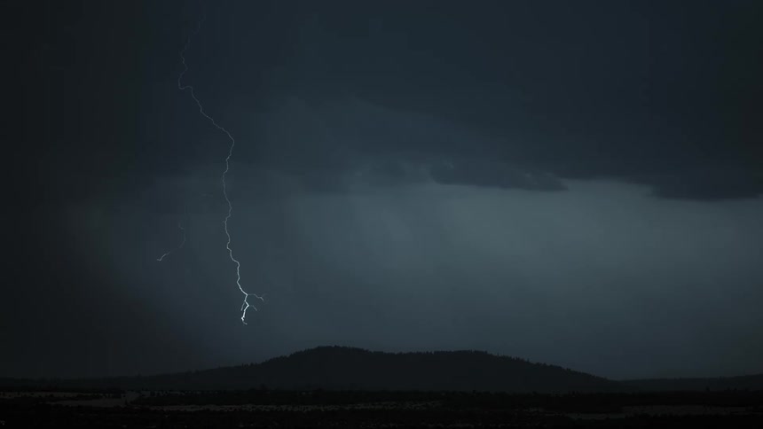 Lightning bolts flash from a dark sky and come down near a mountain