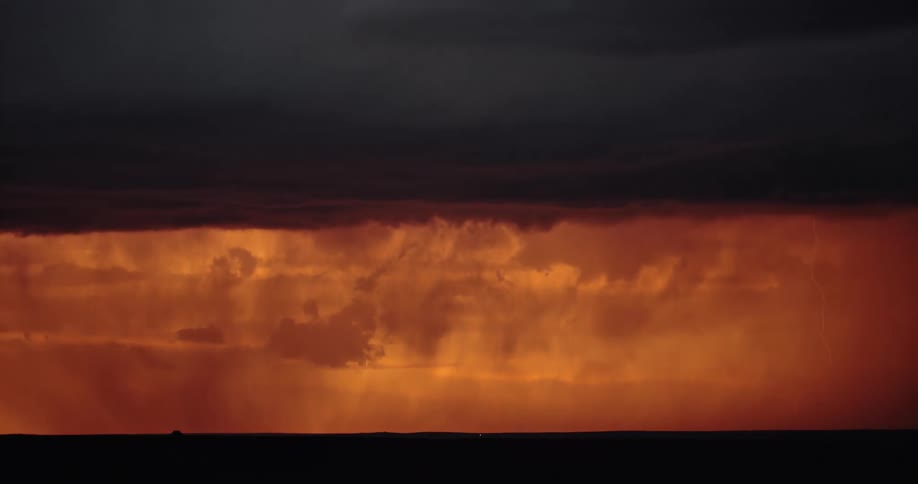 Lightning streaking arcs flashing across storm clouds hitting the ground over a field