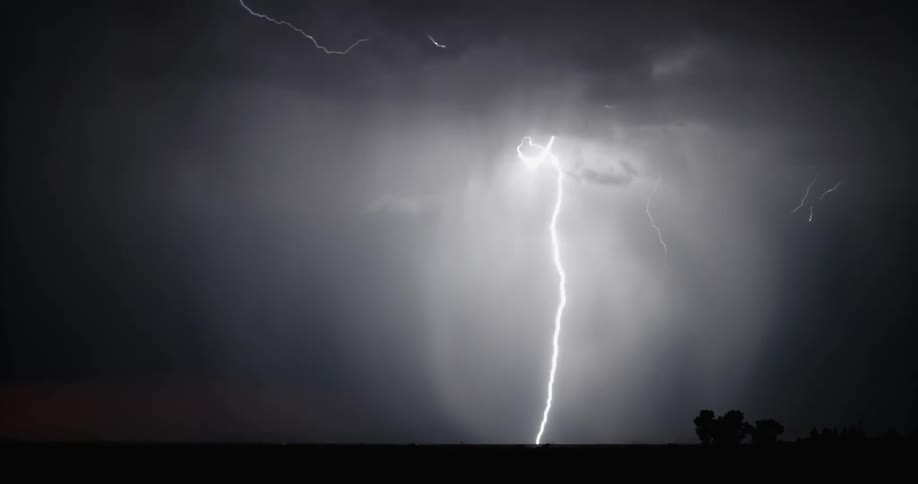 Streaks of lightning flash across a dark sky at nighttime out in a large open field