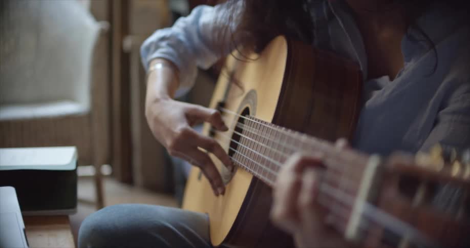 A woman is playing guitar while sitting indoors