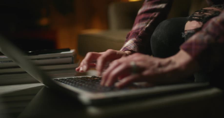 A woman sitting in the living room of a house types on a laptop