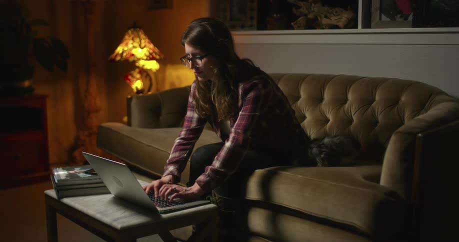 A woman in a room sitting on a couch typing on a laptop