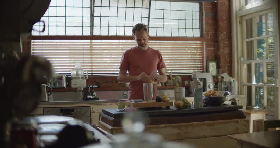 A man peeling a banana next to a blender in a home kitchen