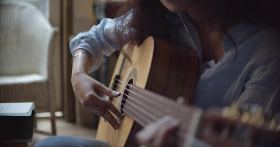 A woman is sitting down and playing the guitar