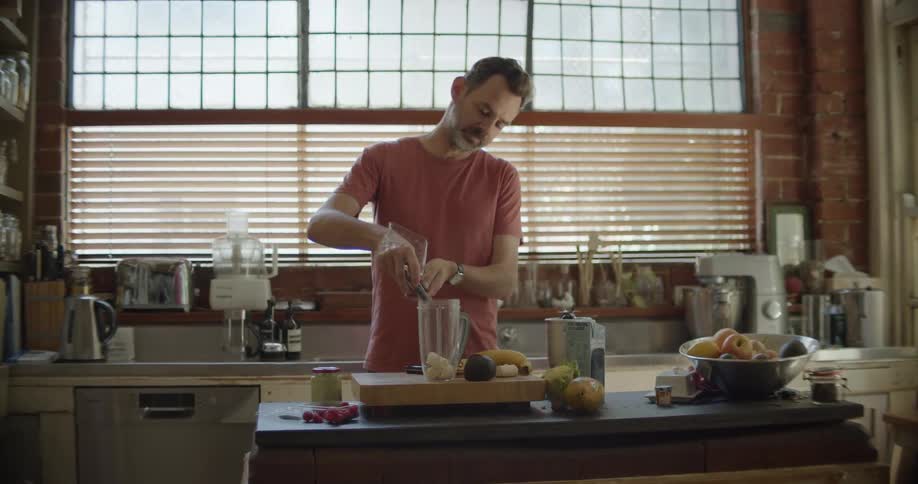Man preparing fresh fruit juice on a blender in the kitchen countertop