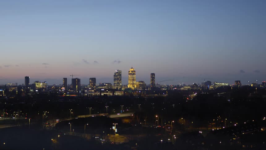 High rise buildings in the distance of a city in the evening with a highway down below where cars are driving by