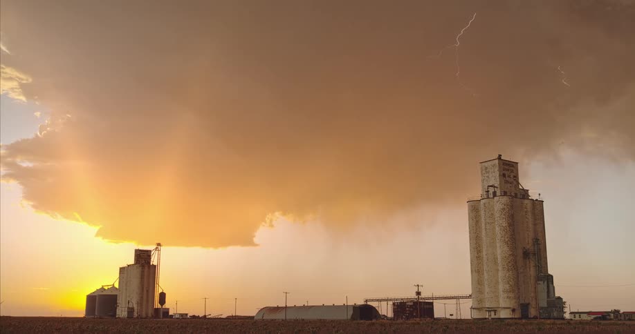 Lightning streaking arcs flashing across yellow storm clouds hitting the ground over the grain silos a field