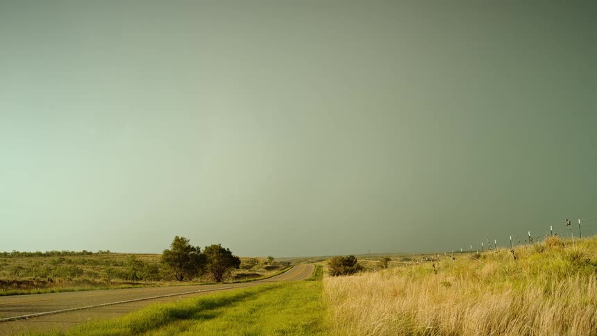 Lightning flashing in the gray cloudy sky over a road through a grassland during the day