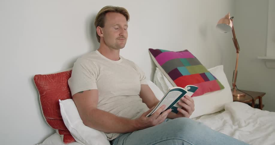 Young muscular man reading a book in bed at home