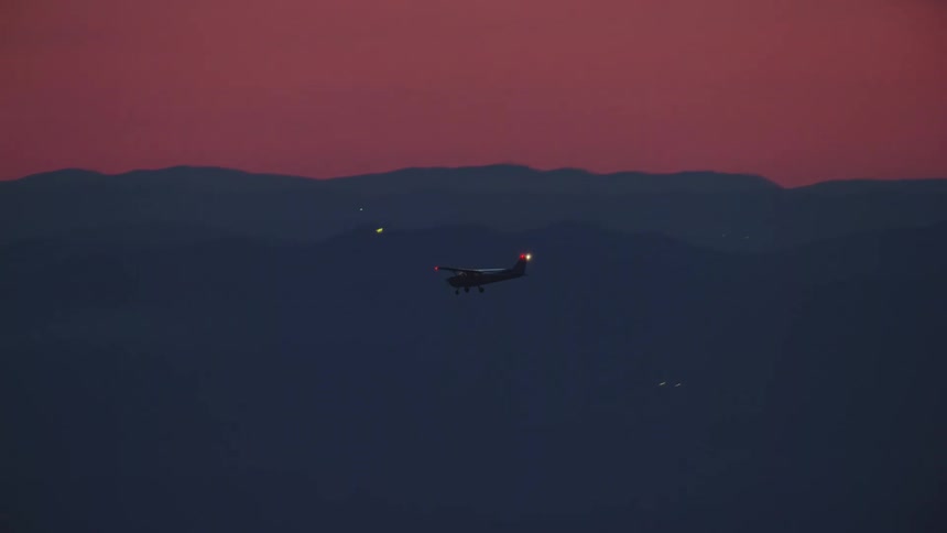 A small single engine white airplane flies in beautiful blue hour magic light in this air to air aerial under a pink sunset sunrise  sky