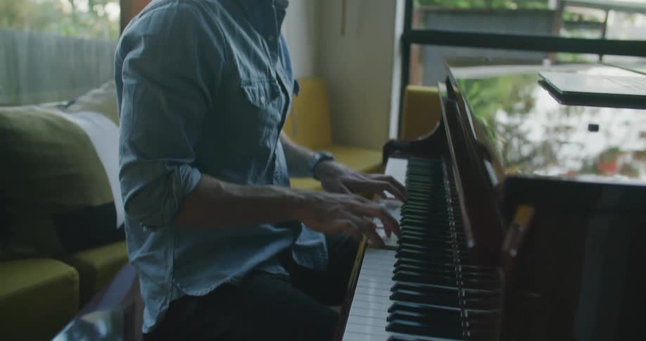 Man using a laptop over a piano to arrange and compose music at home