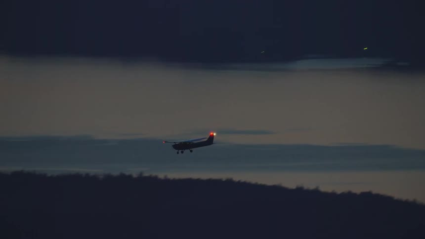 Night air to air aerial of a white single engine airplane crossing from the right side of the frame to the left with anti collision strobe lights flashing