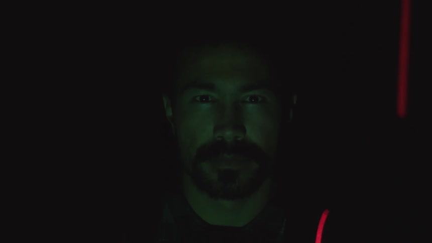 Bearded man looking at the camera having his face scanned by a red laser on a dark room