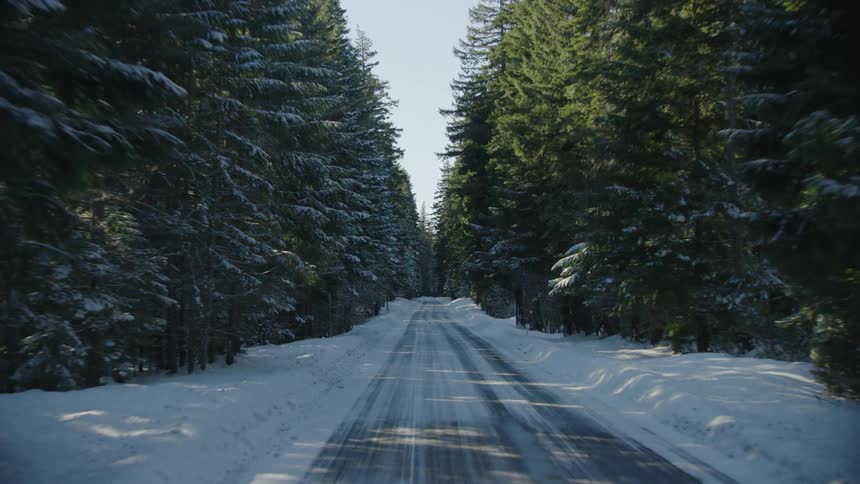 Looking back on a frosted two land road with large snow drifts on the side as the family drives to celebrate Christmas in December at relatives house deep in the woods