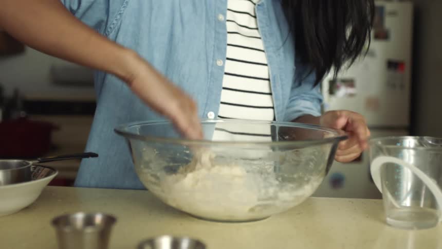 Young woman mixing and kneading dough in a mixing bowl over the kitchen counter top at home