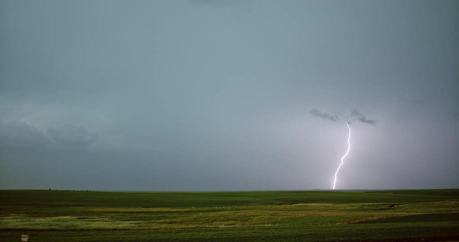 A bolt of lightning strikes down to the ground from storm clouds across a field at daytime