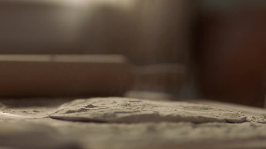 A person mixing flour into dough on a table