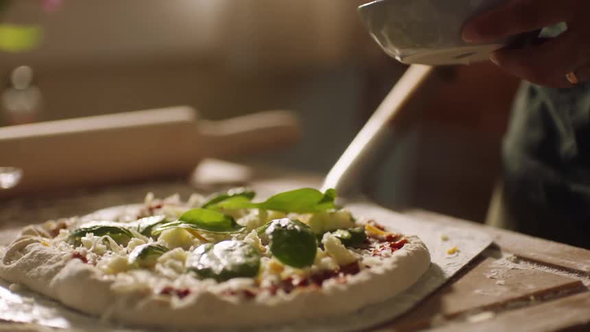 A person puts toppings on a homemade pizza