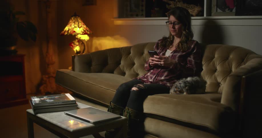 Young woman sitting with a pet dog in a couch at home puts a phone over the coffee table