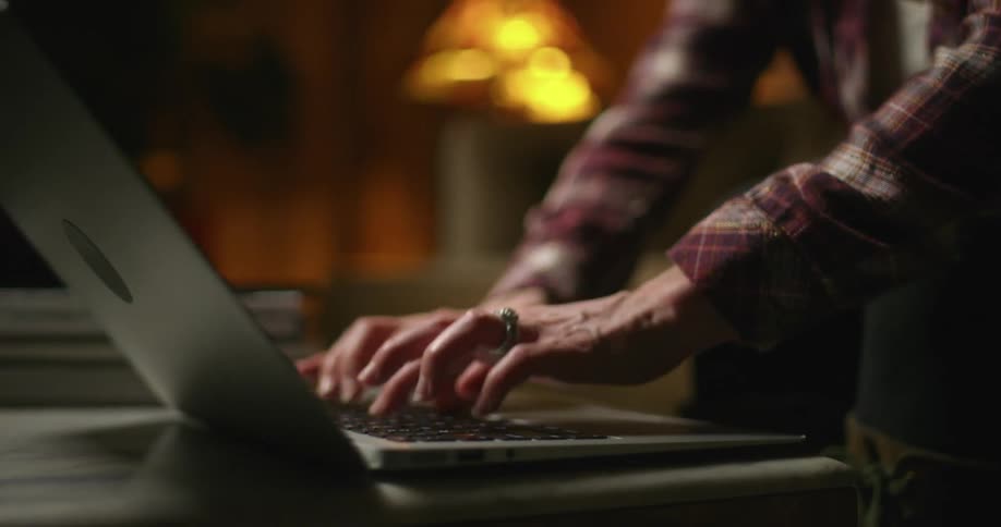 A person typing on the keyboard of a laptop over a coffee table in the living room