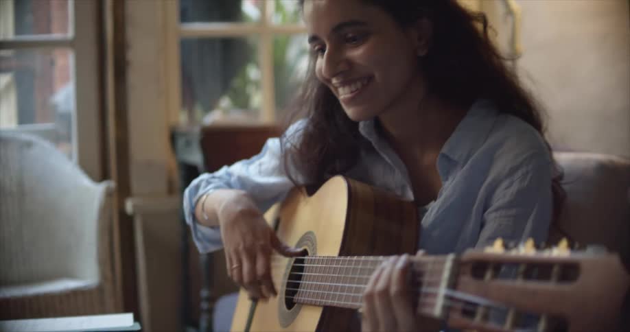 A woman is playing guitar and sitting on a couch
