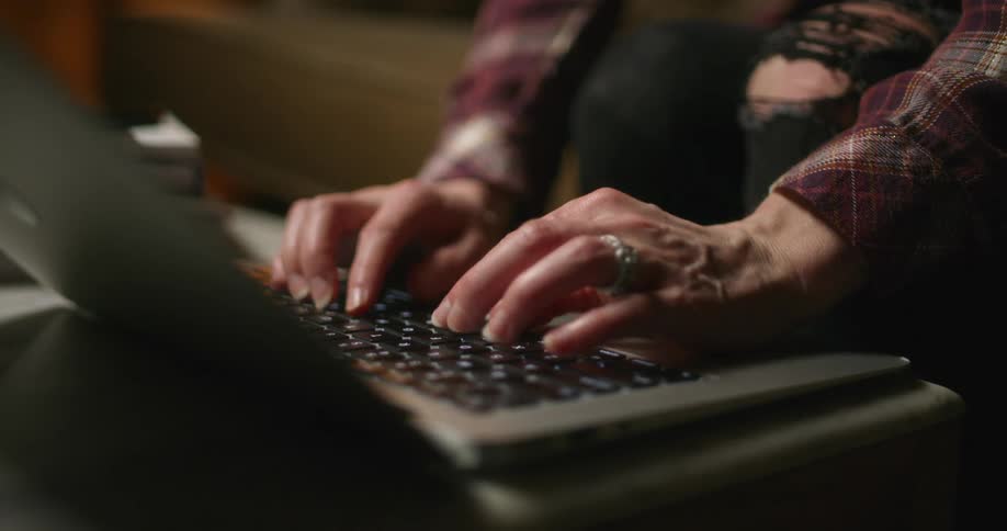 A woman typing on the keyboard of a laptop over a coffee table in the living room