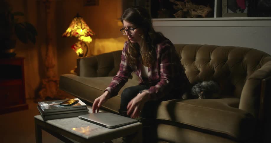 Young woman closes a laptop and stands up from the couch
