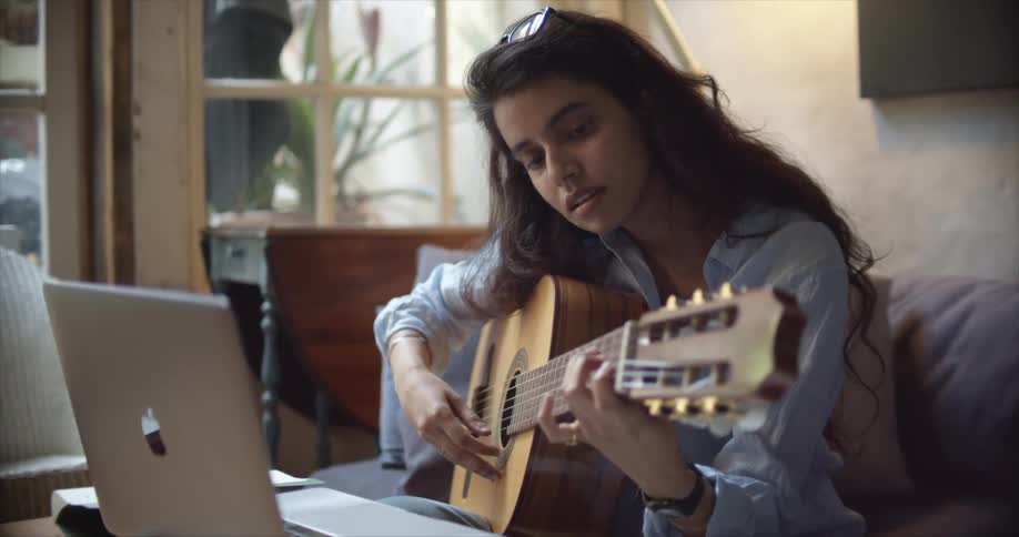 Young woman takes online lessons to learn how to play acoustic guitar at home