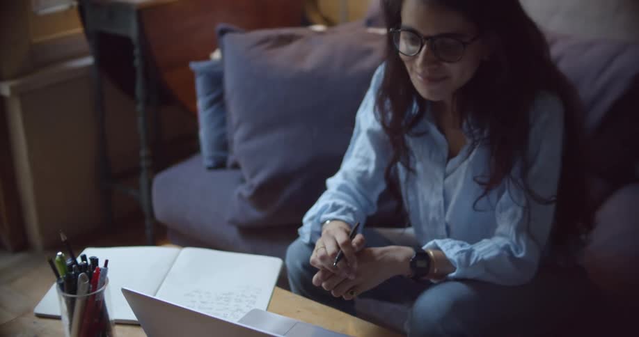A woman sitting on a couch next to a table while video chatting on a laptop
