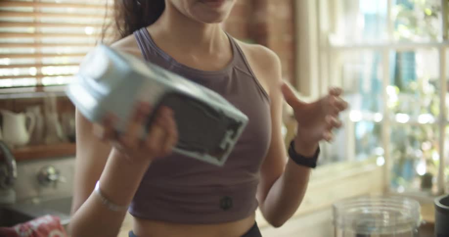 A woman in the kitchen adding fruit and milk into a blender