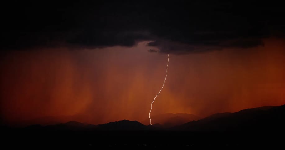 Lightning streaking arcs flashing across red storm clouds hitting the ground over a field