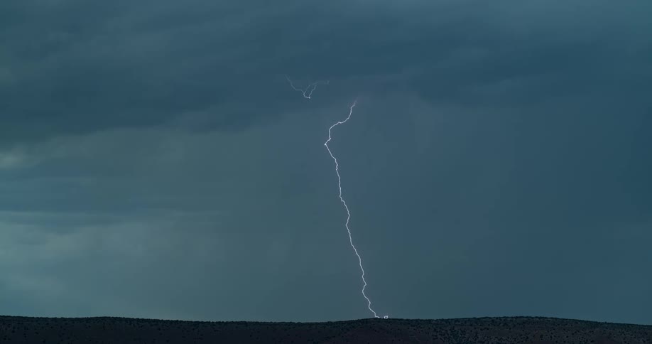 Lightning bolts flash and branch out from storm clouds in dark sky