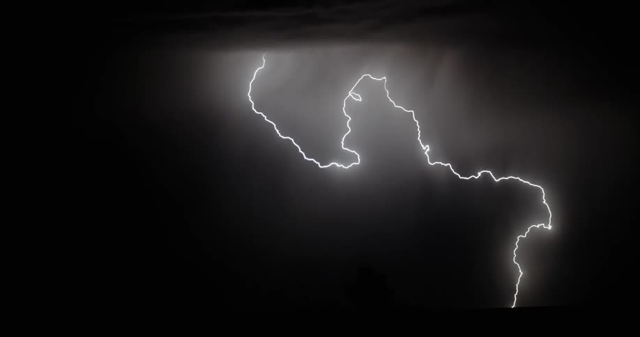 Lightning flashes and spreads through the nighttime sky over a field