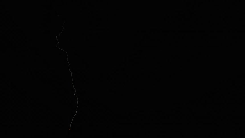 Lightning strikes down to the ground from the sky and forks off into three at nighttime