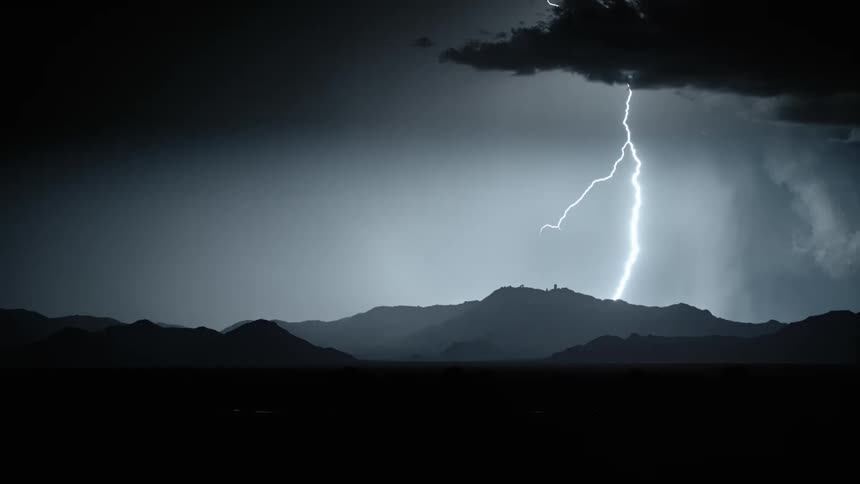 Lightning flashes in a dark sky at night and moves downwards and branches outwards from a straight line