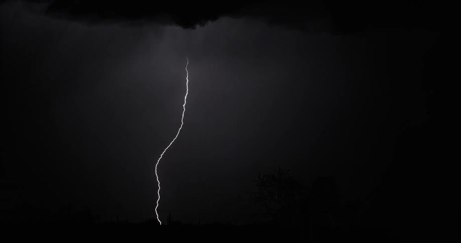 Lightning bolts flash and light up a dark sky under the storm clouds