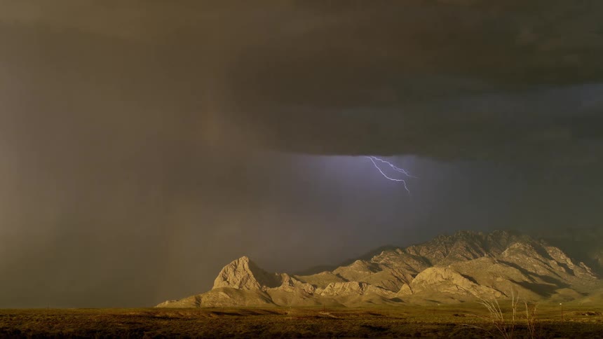 Lightning streaking arcs flashing across storm clouds hitting the ground over the mountains