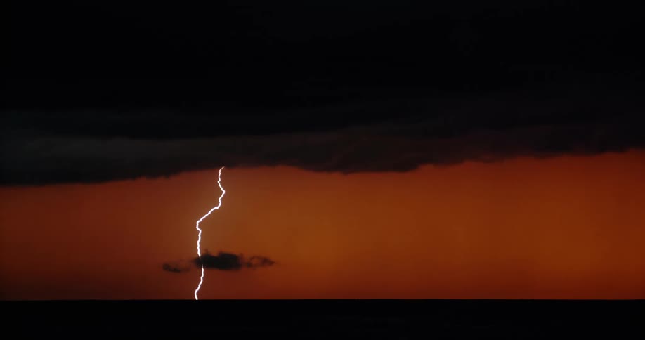 Lightning streaking arcs flashing over the silhouette of black clouds on a red sky