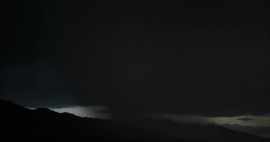 Lightning bolts flash in a dark sky over a mountain range