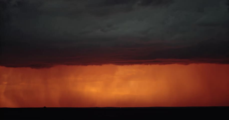 Lightning strikes down from a set of dark clouds in an orange sky in the evening