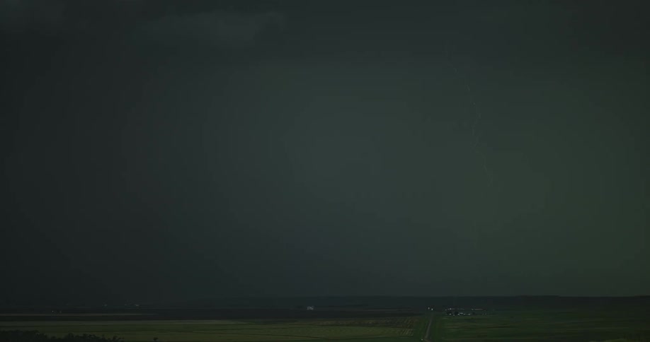 A flash of lightning moves across dark storm clouds in the sky and then strikes down to the ground at nighttime