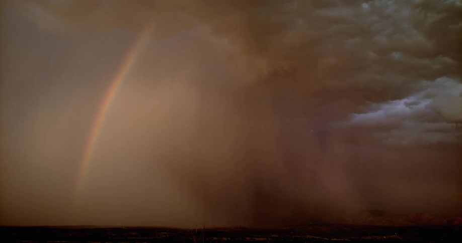 Lightning flashing from storm clouds in an orange sky and a rainbow nearby